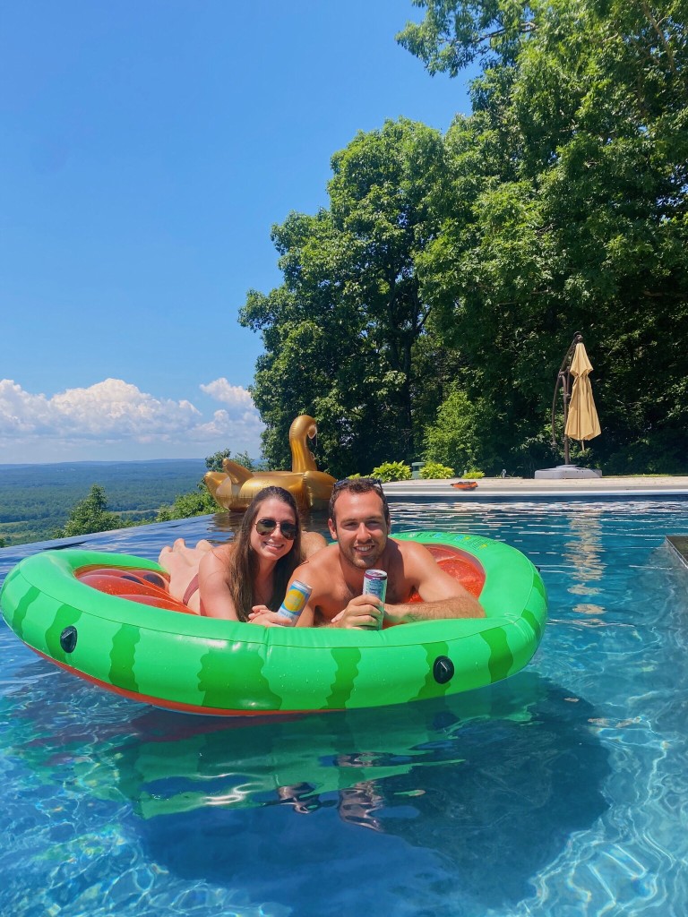 Jenna and Wyatt on a watermelon pool float, smiling in an infinity pool