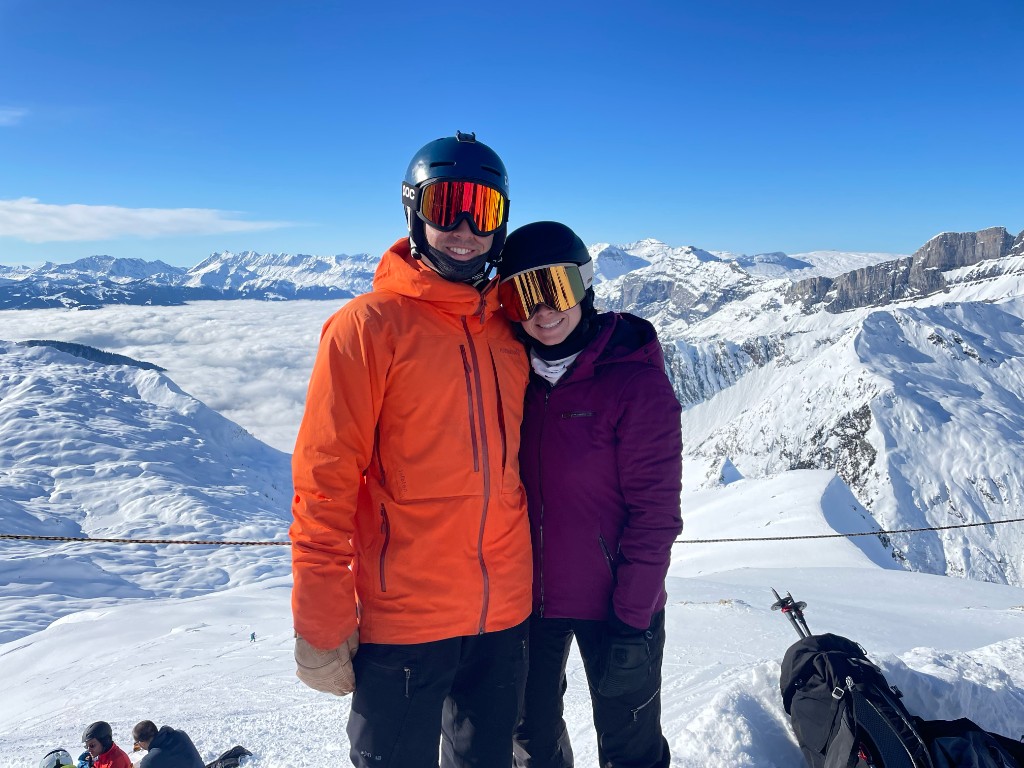 Jenna and Wyatt in ski gear on a snowy mountain peak above the clouds